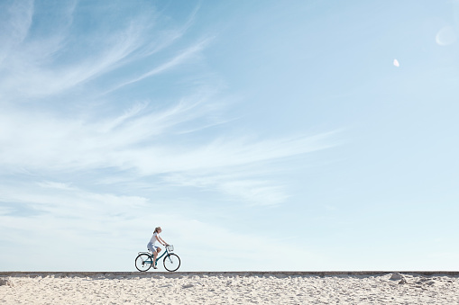 Young woman riding bicycle with basket against blue sky during summer - healthy lifestyle concept