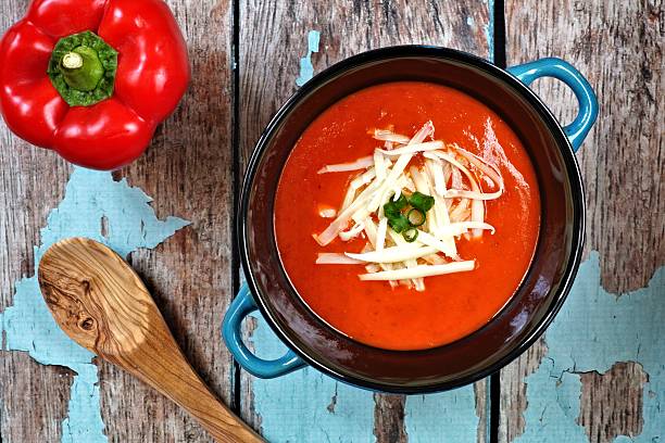 Red pepper soup overhead scene on rustic blue wood background Red pepper soup topped with shredded cheese and green onions, overhead scene on rustic blue wood background shredded mozzarella stock pictures, royalty-free photos & images