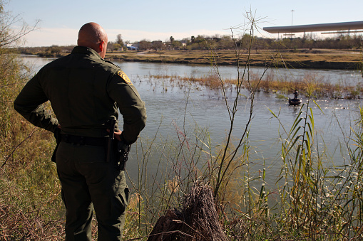 Rio Grande City, Texas, USA - February 9, 2016: A Border Patrol agent watches a Mexican man with an inner tube used to transport illegal aliens across the Rio Grande River in the Rio Grande Valley in far south Texas. A continuous game of cat and mouse plays out along the river twenty four hours a day.