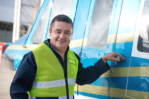 Man working at an airplane hangar opening the door of a plane and looking at the camera smiling