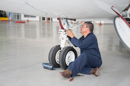 Latin American man fixing the landing gear of a plane at an airplane hangar