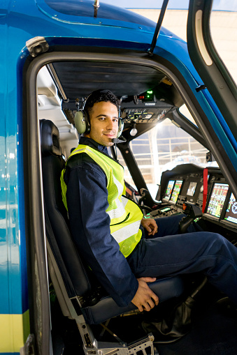 Handsome male pilot flying a helicopter and wearing headset while looking at the camera