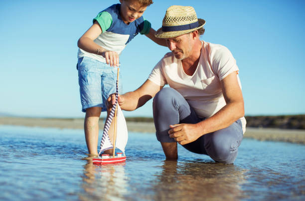 nonno e nipote che giocano con la barca giocattolo in acqua - wading child water sport clothing foto e immagini stock