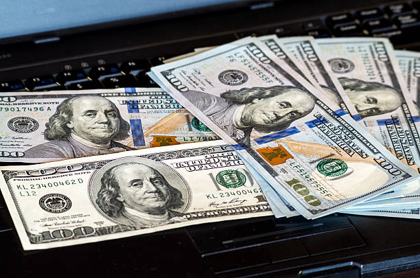 Pack of one hundred dollars notes thrown on laptop keyboard stock photo