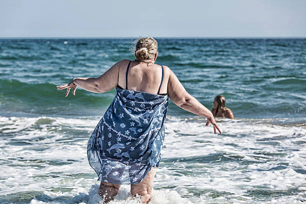 It is Cold Water A senior woman reacts to the cold water as she walks out in the ocean (filtered) woman cold water swimming stock pictures, royalty-free photos & images