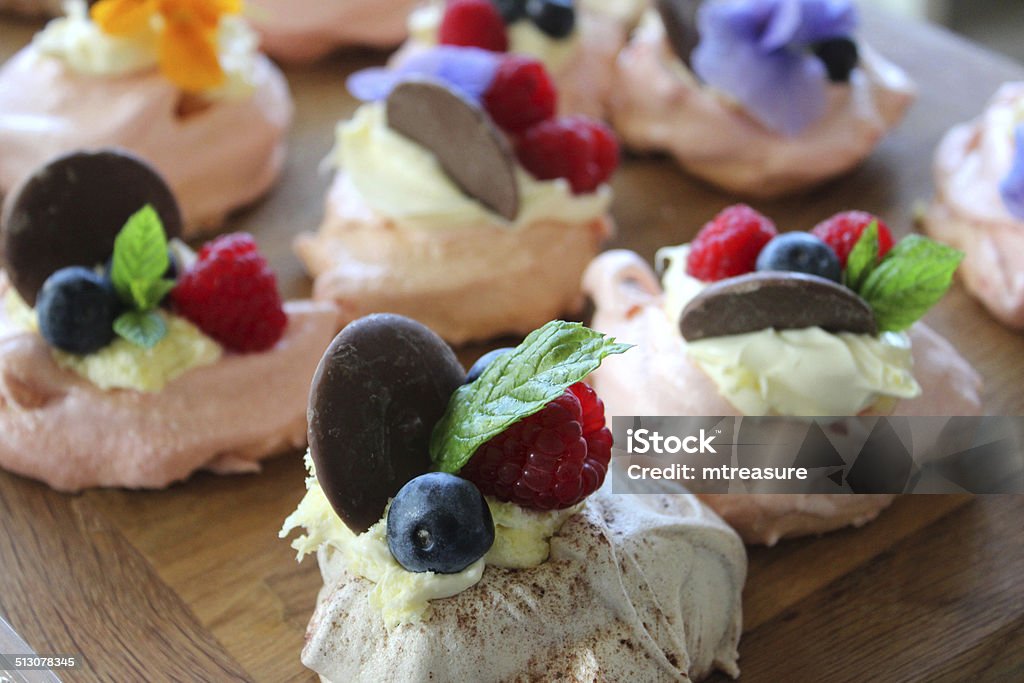 Homemade pink meringues decorated with cream, chocolate, fruit, edible flowers Photo showing a group of homemade pink meringues, decorated with fresh cream, chocolate buttons, edible flowers (yellow and blue pansies / nasturtiums), sprigs of fresh mint and berries / fruit, such as fresh raspberries, blackberries and blueberries. Berry Stock Photo