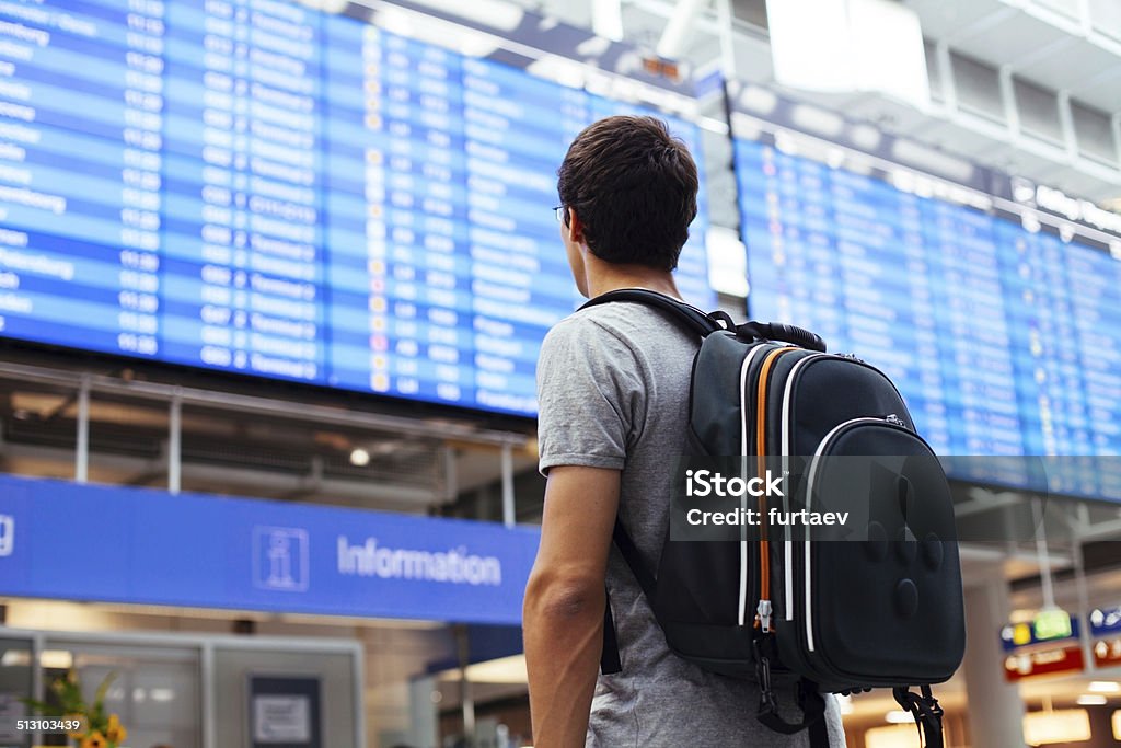 Guy near airline schedule Young man with backpack in airport near flight timetable Airport Stock Photo