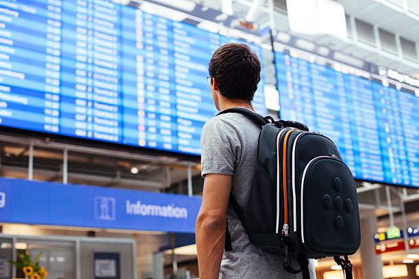 Guy near airline schedule Young man with backpack in airport near flight timetable arrival departure board photos stock pictures, royalty-free photos & images