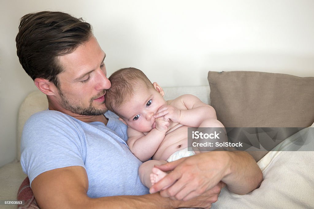 Father and Baby Daughter Father relaxing on a sofa with baby daughter in his arms sucking her thumb 0-11 Months Stock Photo