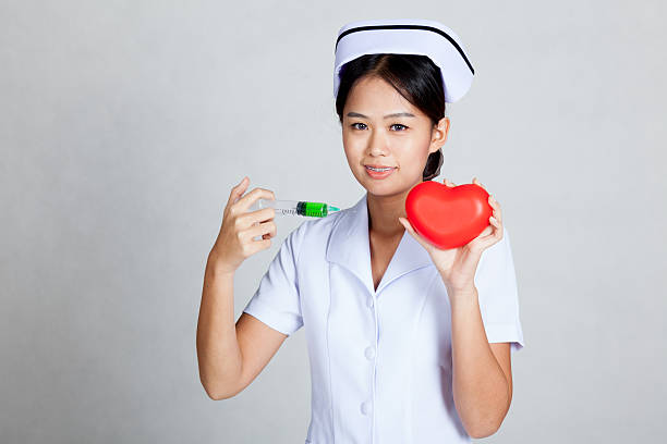 Asian young nurse hold syringe and red heart on gray background