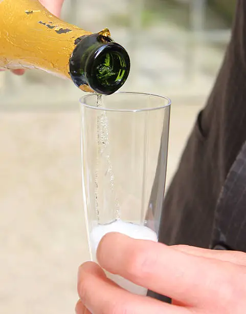 Close-up photo showing a newly married bridegroom pouring himself some champagne / sparkling wine into an elegant champagne glass / flute, ready to toast his new bride.