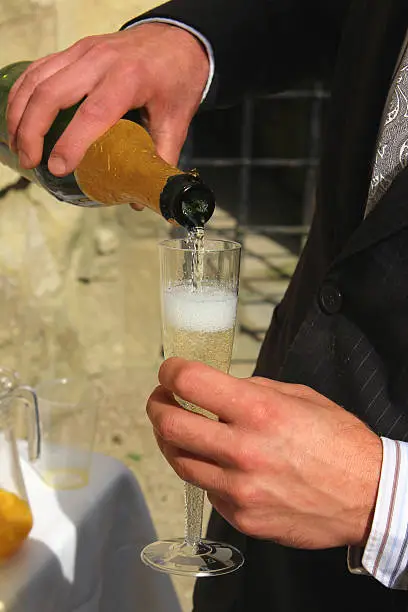 Photo showing a newly married bridegroom pouring himself some champagne into an elegant champagne glass / flute, ready to toast his new bride.