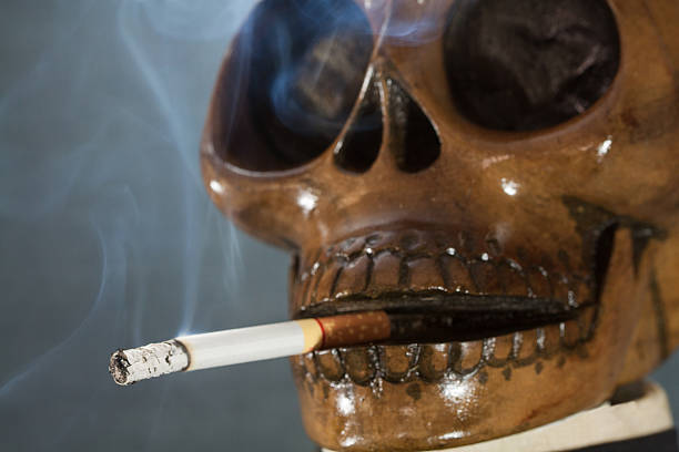 человеческий череп курение сигарет на черном фоне - cigarette addiction shock smoking стоковые фото и изображения