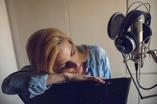 Tired young woman taking a break from recording and relaxing while leaning on music stand with her eyes closed.