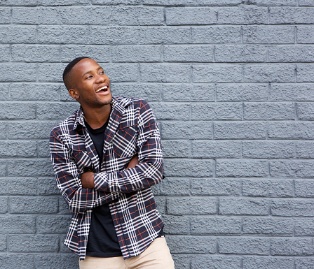 Portrait of a happy young black man smiling with arms crossed against gray wall