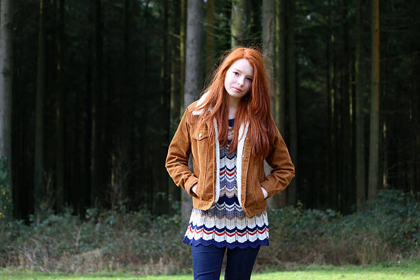 Image of attractive girl, long red hair, hands in pockets Photo showing a three-quarter length image of an attractive, teenage girl with long, flowing, red hair. This picture shows the teenager walking through a woodland wearing a brown, corduroy jacket. cute 15 year old girls stock pictures, royalty-free photos & images