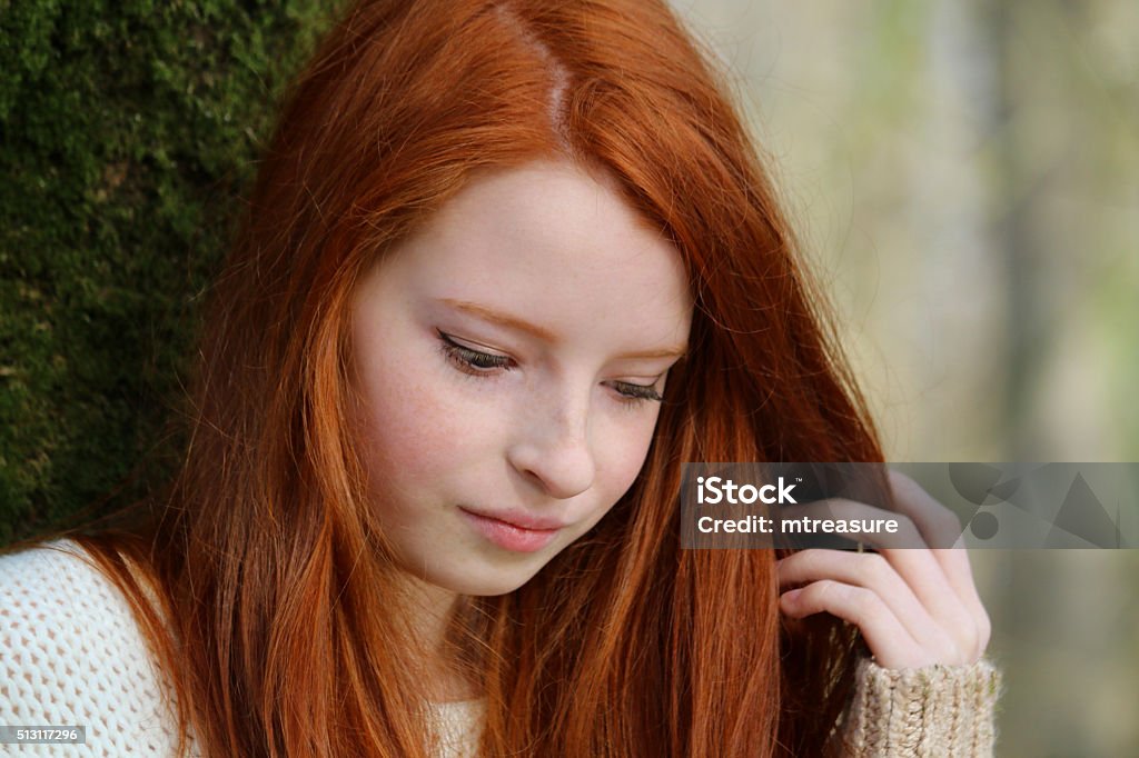 Stock head shot image of pretty red haired girl, looking-down Photo showing a portrait of an attractive, teenage girl with long, flowing, red hair. This picture shows the teenager leaning against the trunk of a tree in a deciduous wood. 14-15 Years Stock Photo