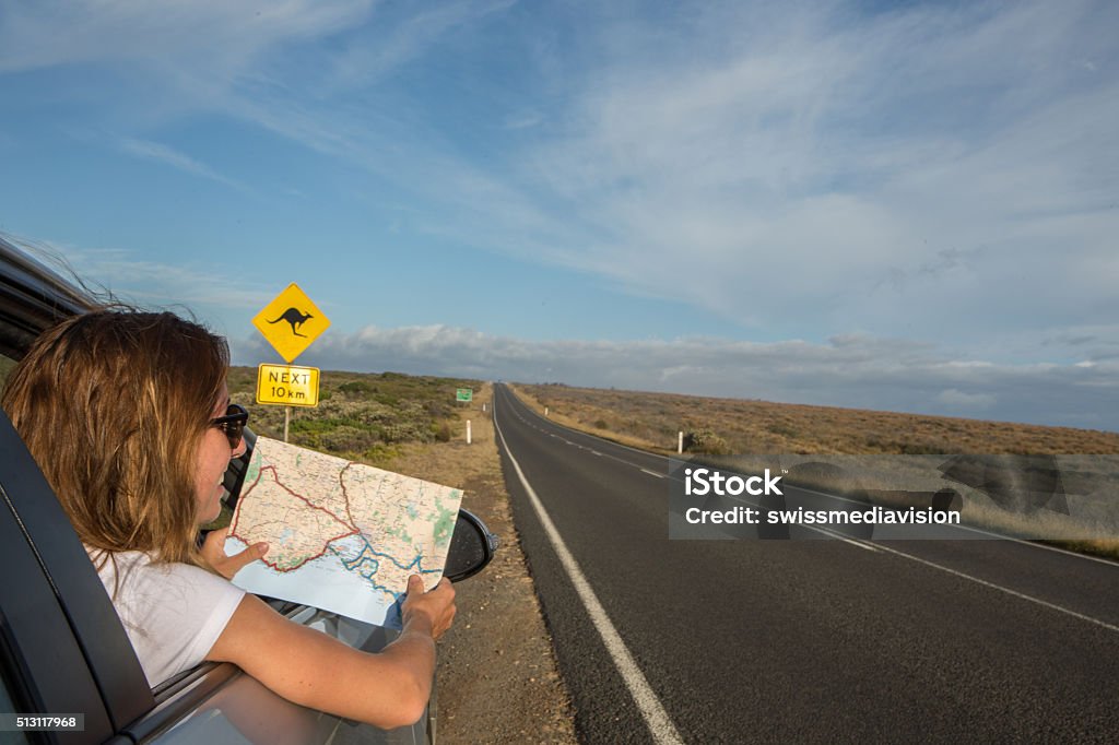 Young woman in a car reads a road map-Australia Young woman in a car on the roadside reads a road map. Kangaroo warning sign ahead. Australia Stock Photo