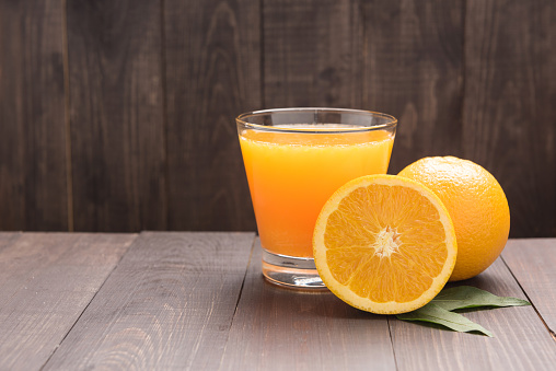 Fresh orange juice and oranges on wooden table.