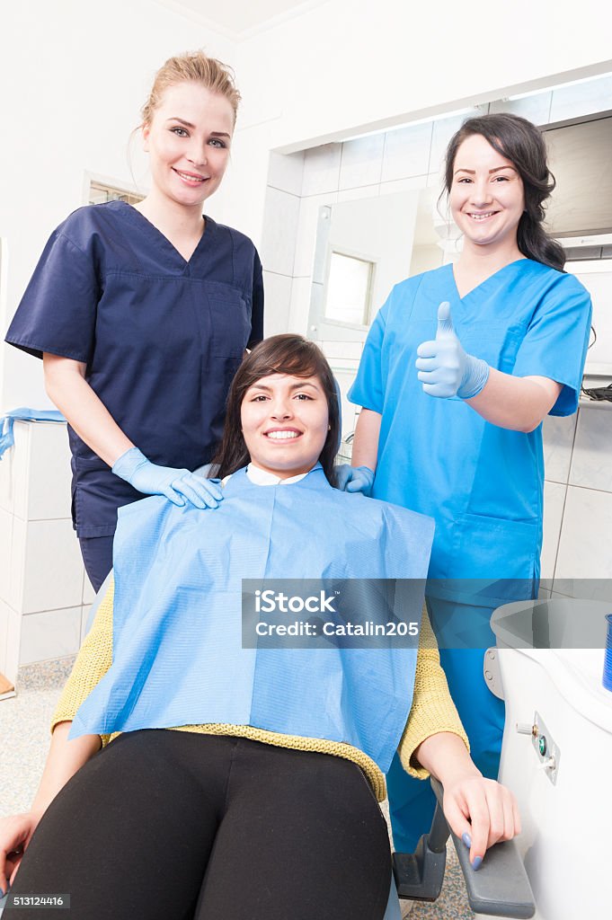 Friendly dentist with smiling patient and assistant showing thum Friendly dentist with smiling patient and assistant showing thumb up in dental office Adult Stock Photo