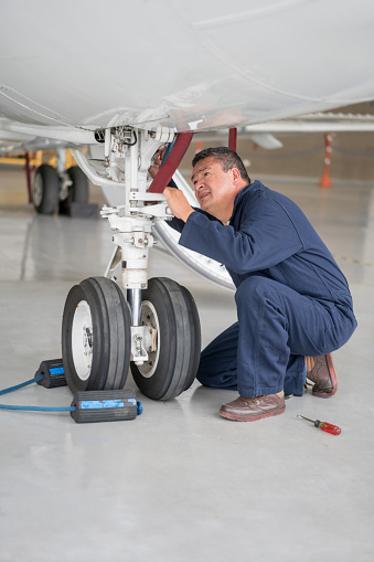 Mechanic repairing landing gear of an airplane at the hangar - people at work concepts