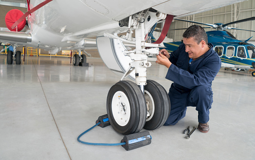 Happy Latin American mechanic working at an airplane hangar and fixing the landing gear of a plane