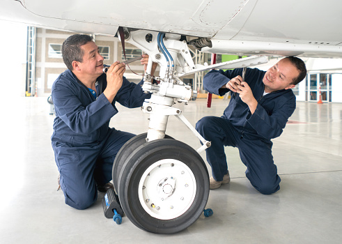 Team of mechanics working at an airplane hangar fixing the landing gear of a plane