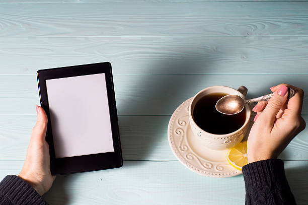Female hands hold e-book on blue wooden background.