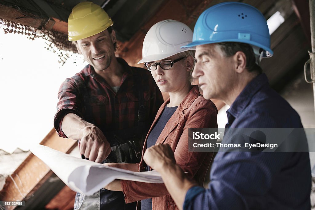 Construction Foreman with Blueprints Construction foreman pointing out details on building blueprints. Architects are with him looking over the plans. Location is a real construction site. 25-29 Years Stock Photo