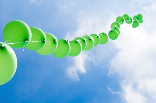 Green balloons on a string and cloudy sky