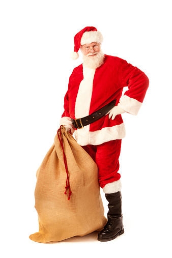 Subject: A sideview of Santa Claus as he carries a heavy burlap bag of Christmas gifts over his shoulder, on his back. Isolated on a white background.