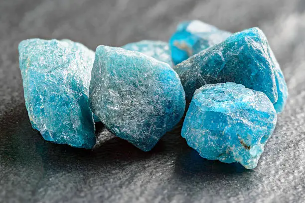 Blue, uncut apatite gemstone crystals on black stone plate.