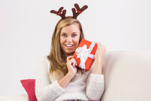 Festive blonde relaxing on sofa with gift at home in the living room