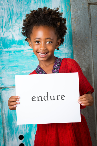 Adorable Ethiopian child holding 'endure' sign outdoors