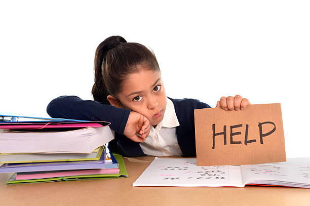 sweet little girl bored under stress with tired facial expression sweet little female latin child studying on desk asking for help holding cardboard message looking bored and under stress with a tired face expression in children education and back to school concept isolated on white background struggle stock pictures, royalty-free photos & images