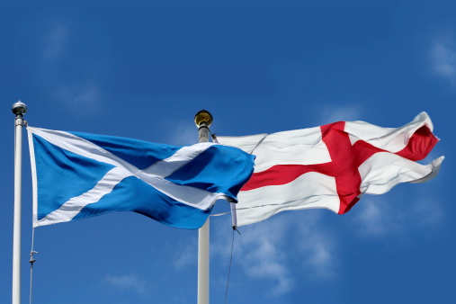Scottish and English flags flutter in the breeze against a blue sky