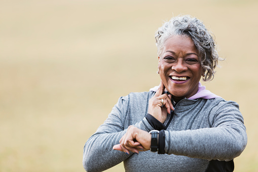 African American senior woman (60s) exercising outdoors, taking pulse.