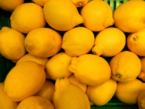 Photo showing a stack of fresh, ripe, unwaxed lemons, piled high in a green plastic crate at a supermarket / fruit shop.  This yellow citrus fruit is organic and was imported from Asia.