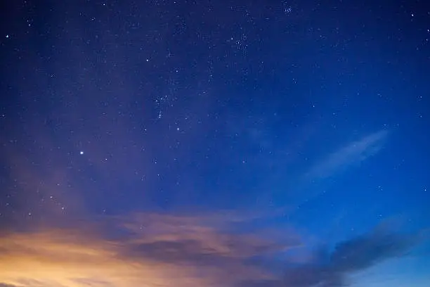 night sky with clouds and stars and constellations.  light from albuquerque colors the clouds.  horizontal wide angle composition with copy space taken in the ojito wilderness.  new mexico.