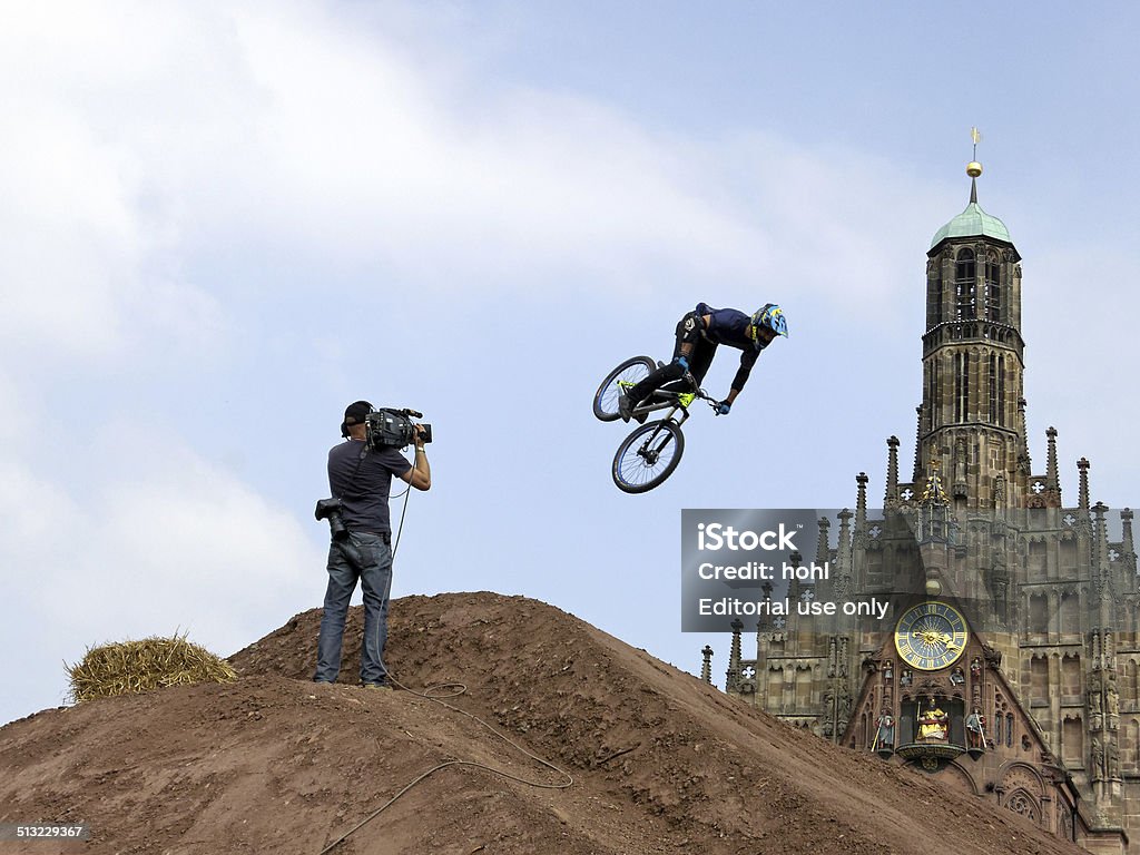 flying cyclist - "District Ride" in Nuremberg Nuremberg, Germany - September 5, 2014: A cyclist is making a somersault with his bicycle in front of the famous gothic Frauenkirche at the marketplace  in Nuremberg. The cyclist is filmed by a cameraman at the freeride event "District Ride". The freeride event "District Ride" is organized by the austrian company Red Bull and takes place in 2014 for the 3rd time in Nuremberg. Activity Stock Photo