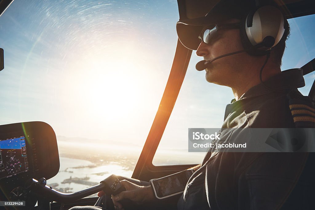 Pilot flying a helicopter on a sunny day Close up of a pilot flying a helicopter with sun flare entering the cockpit. Pilot Stock Photo