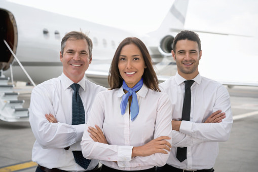 Cabin crew of a private airplane at the airport looking at the camera smiling