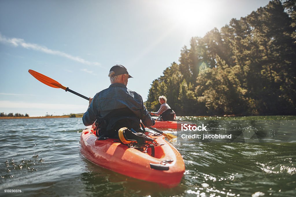 Couple kayaking in the lake on a sunny day Outdoor shot of mature man canoeing in the lake with woman in background. Couple kayaking in the lake on a sunny day. Kayaking Stock Photo