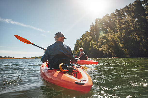 Couple kayaking in the lake on a sunny day Outdoor shot of mature man canoeing in the lake with woman in background. Couple kayaking in the lake on a sunny day. kayaking stock pictures, royalty-free photos & images