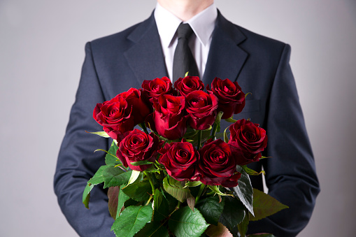 Man with bouquet of red roses on a gray background. Present at the International Women's Day