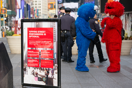 New York, USA - January 15, 2016: People dressed as Cookie Monster and Elmo in Times Square late in the day, standing next to NYPD Officers and a warning sign letting tourist know tipping is optional. The signs were put in place after reports of aggressive street performers demanding money from tourist.