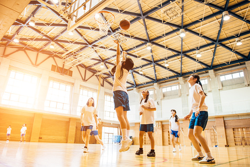 Basketball female team throwing ball into hoop while training at indoor sports court wide shot