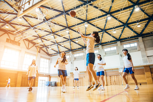 Japanese Junior High School girl friends playing basketball in the School GYM.
