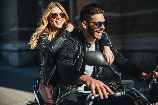 Brutal young man in sunglasses, blue jeans and a black leather jacket sitting on the custom motorcycle outdoor