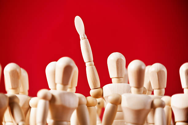 istock Me! I'll do it! One puppet in crowd raises hand 513253651